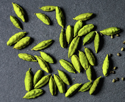 Green cardamom pods scattered on a dark textured slate background.